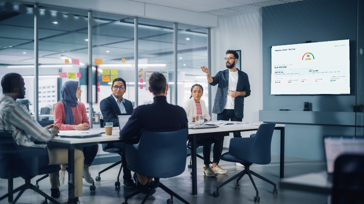 A leadership team around a table working through a scenario together, with their tabletop debrief on the screen behind them.